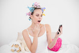 Surprised natural brown haired woman in hair curlers looking at her mobile phone