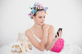 Stern natural brown haired woman in hair curlers looking at her mobile phone