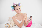 Happy natural brown haired woman in hair curlers holding a mobile phone