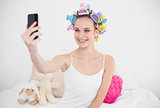 Pretty natural brown haired woman in hair curlers taking a picture of herself with mobile phone