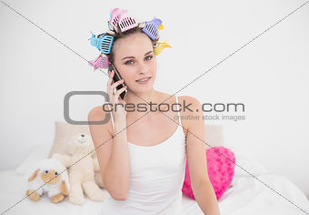 Thoughtful natural brown haired woman in hair curlers making a phone call