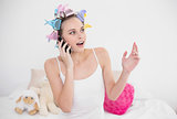 Surprised natural brown haired woman in hair curlers making a phone call