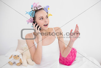 Surprised natural brown haired woman in hair curlers making a phone call
