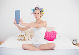 Pouting natural brown haired woman in hair curlers taking picture of herself with a tablet