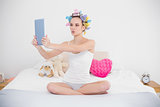Funny natural brown haired woman in hair curlers taking picture of herself with a tablet