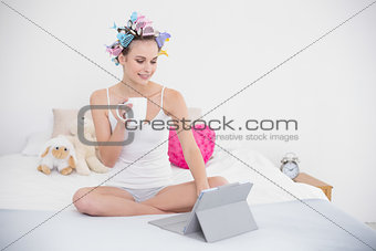 Concentrated natural brown haired woman in hair curlers using a tablet pc