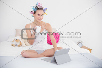 Stern natural brown haired woman in hair curlers holding a cup of coffee