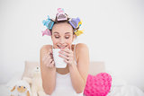 Funny natural brown haired woman in hair curlers enjoying coffee smell