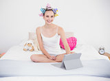 Happy natural brown haired woman in hair curlers using a tablet pc