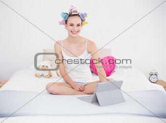 Happy natural brown haired woman in hair curlers using a tablet pc