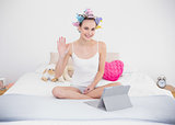 Joyful natural brown haired woman in hair curlers chatting online with a tablet pc