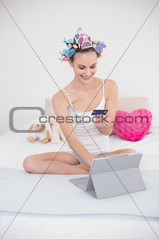 Content natural brown haired woman in hair curlers shopping online with her tablet pc