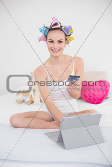 Pleased natural brown haired woman in hair curlers shopping online with her tablet pc