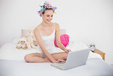 Happy natural brown haired woman in hair curlers using a laptop