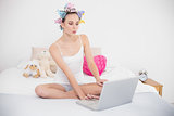 Pouting natural brown haired woman in hair curlers using a laptop