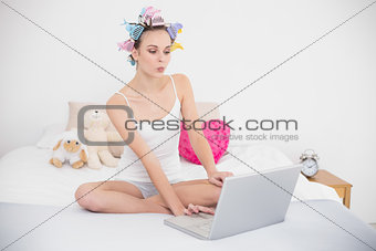 Pouting natural brown haired woman in hair curlers using a laptop