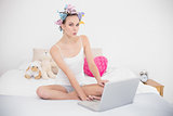 Funny natural brown haired woman in hair curlers using a laptop