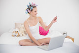 Beautiful natural brown haired woman in hair curlers shopping online with a laptop