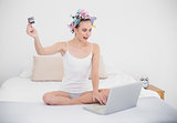 Amazed natural brown haired woman in hair curlers shopping online with a computer