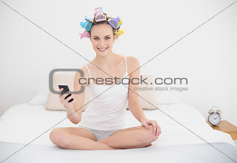 Content natural brown haired woman in hair curlers holding a mobile phone