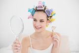 Beautiful natural brown haired woman in hair curlers looking herself in a mirror