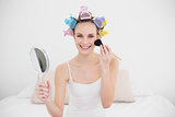 Joyful natural brown haired woman in hair curlers applying powder on her face