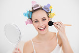 Smiling natural brown haired woman in hair curlers applying powder on her face