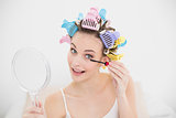 Cheerful natural brown haired woman in hair curlers applying mascara