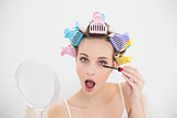 Concentrated natural brown haired woman in hair curlers opening her mouth while applying mascara