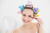 Pretty natural brown haired woman in hair curlers applying mascara