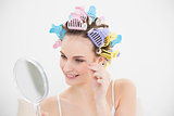Cute natural brown haired woman in hair curlers plucking her eyebrows