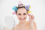 Charming natural brown haired woman in hair curlers plucking her eyebrows