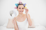 Amused natural brown haired woman in hair curlers plucking her eyebrows