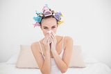 Cute natural brown haired woman in hair curlers sneezing in a tissue