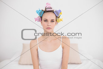 Upset natural brown haired woman in hair curlers looking at camera