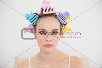 Stern natural brown haired woman in hair curlers looking at camera