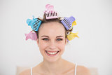 Smiling natural brown haired woman in hair curlers looking at camera