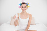 Cheerful natural brown haired woman in hair curlers holding a glass of water