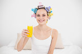 Charming natural brown haired woman in hair curlers holding a glass of orange juice