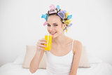 Cute natural brown haired woman in hair curlers drinking orange juice