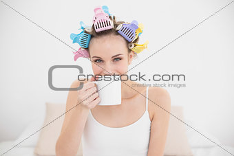 Delighted natural brown haired woman in hair curlers enjoying coffee smell