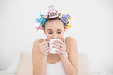 Peaceful natural brown haired woman in hair curlers enjoying coffee smell