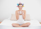 Pretty natural brown haired woman in hair curlers holding a mug of coffee