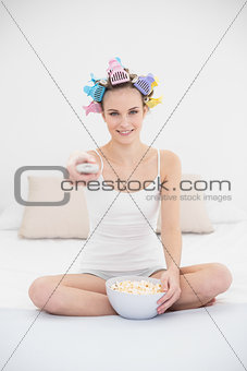 Concentrated natural brown haired woman in hair curlers watching tv while eating popcorn