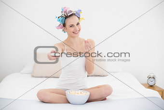 Delighted natural brown haired woman in hair curlers eating popcorn while watching tv
