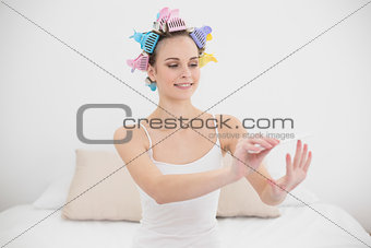 Concentrated natural brown haired woman in hair curlers filing her nails