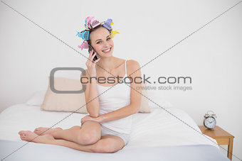 Amused natural brown haired woman in hair curlers making a phone call
