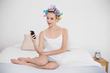 Amazed natural brown haired woman in hair curlers looking at her mobile phone