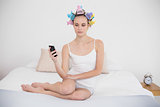 Frowning natural brown haired woman in hair curlers looking at her mobile phone