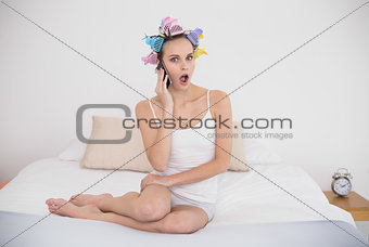 Astonished natural brown haired woman in hair curlers answering her mobile phone